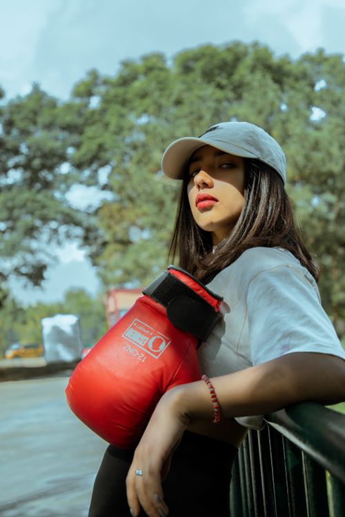 Free Confident young woman wearing a white cap and holding red boxing gloves outdoors. Stock Photo