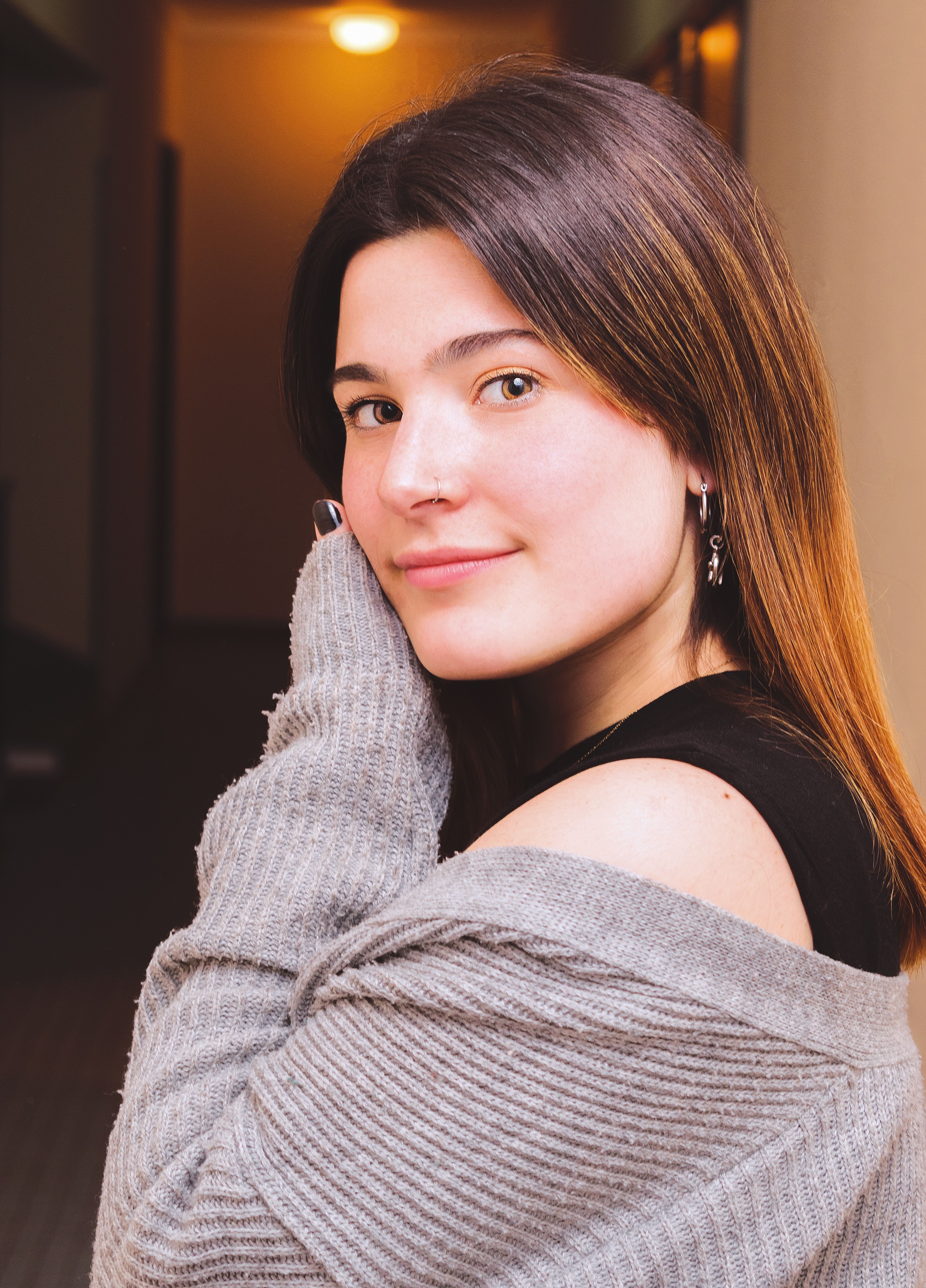 A candid portrait of a woman with a gentle smile wearing a cozy gray sweater indoors.