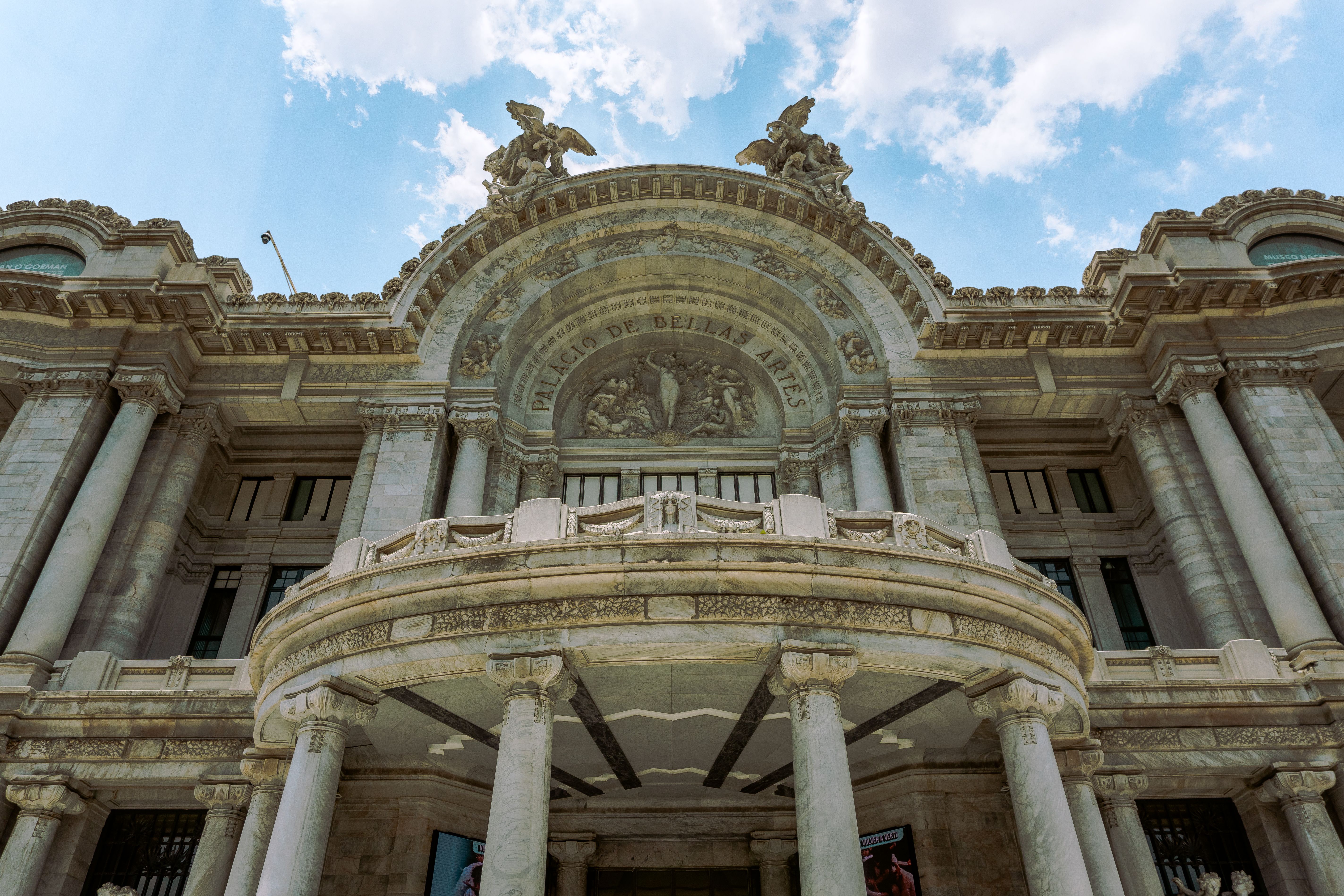 Low angle view of the grand Palacio de Bellas Artes with architectural details under a clear blue sky.