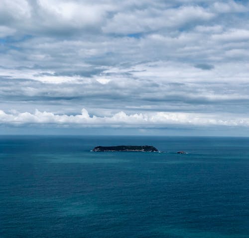A Small Island on the Middle of the Sea Under Cloudy Sky