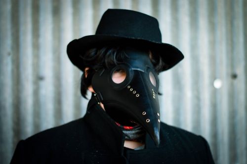 Free Portrait of a person wearing a plague doctor mask and black hat against a textured wall. Stock Photo