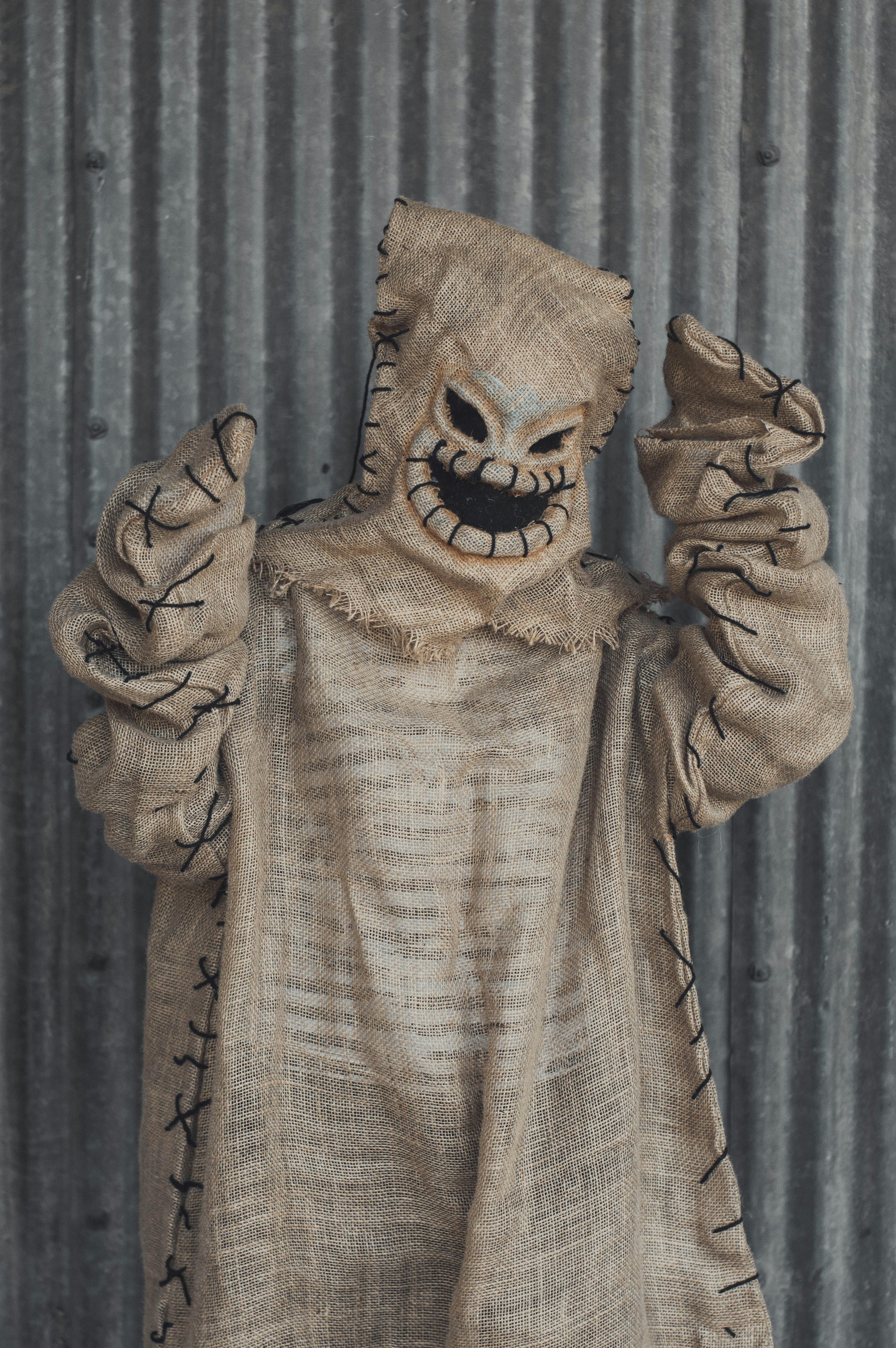 Free A person in a spooky burlap costume poses eerily against a metal background. Stock Photo