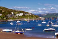 在郁郁葱葱的山丘和清澈的蓝天背景下，一个充满活力的沿海码头停泊着帆船