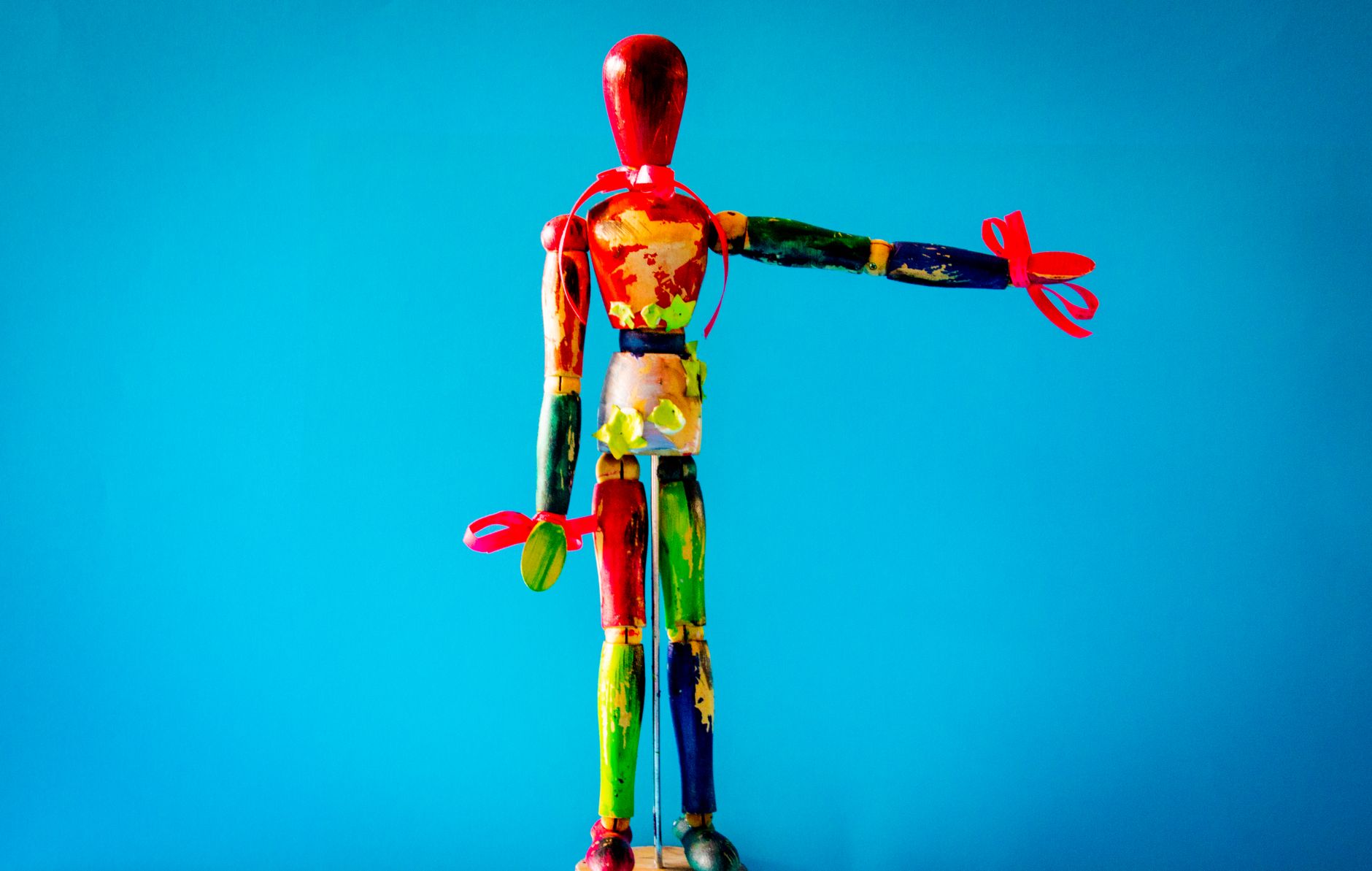 Vibrant wooden mannequin with artistic paint against a blue backdrop.