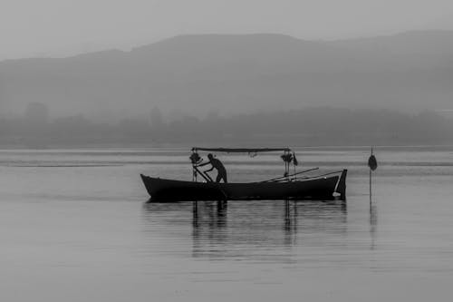 Grayscale Photography of a Man Riding on a Boat on a River