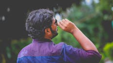 男子身穿紫色衬衫，一边抬头看户外，一边调整太阳镜