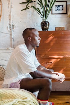 Man seated in a contemporary bedroom, enjoying a serene morning in pajamas.