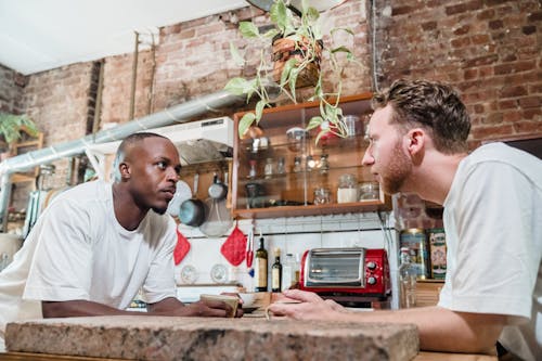 Men Having Coffee and Looking at Each Other in a Kitchen 