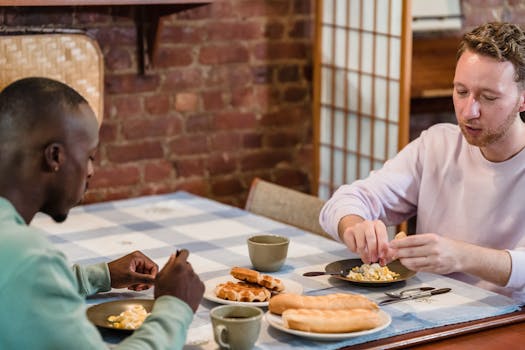 Two men having a casual breakfast with eggs and baguette in a cozy kitchen setting.