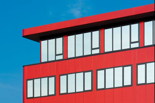 Free A vibrant red building facade with clean lines and large windows set against a clear blue sky. Stock Photo