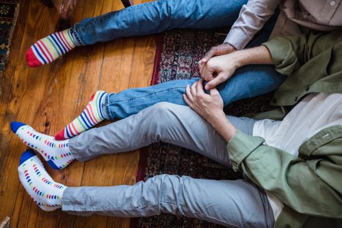 Free Top view of a couple holding hands on a wooden floor, showcasing colorful socks and blue jeans. Stock Photo