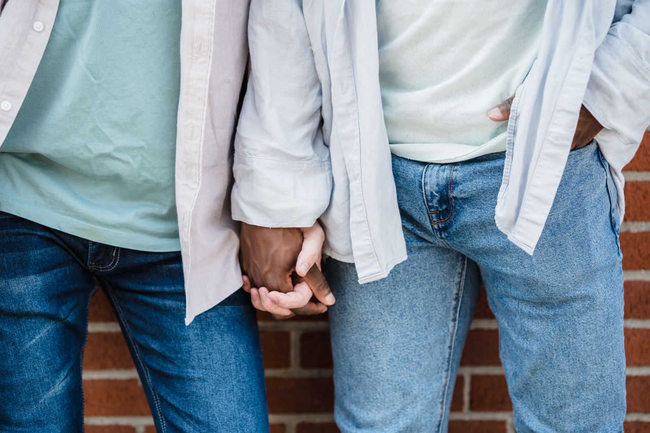 a close up shot of a gay couple holding hands wearing casual jeans and