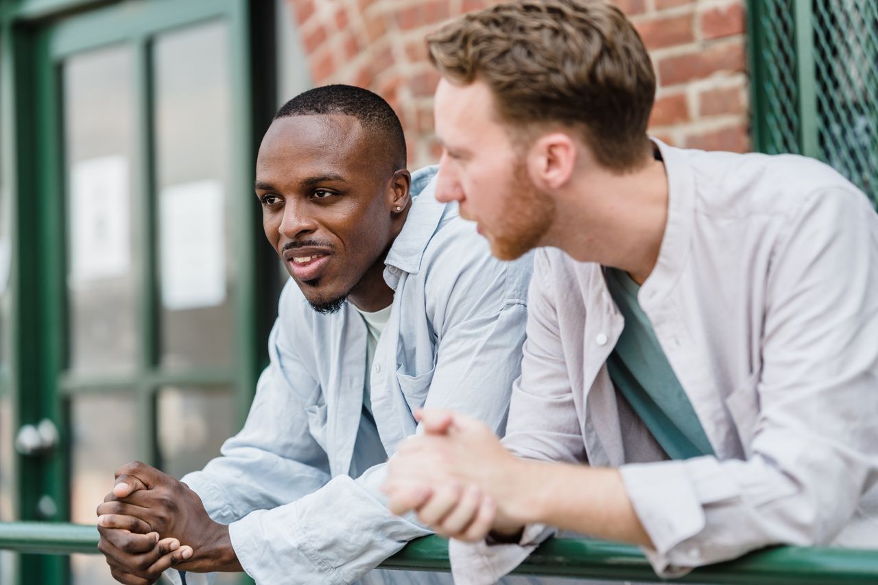 two young men chatting and smiling while leaning on a railing outdoors