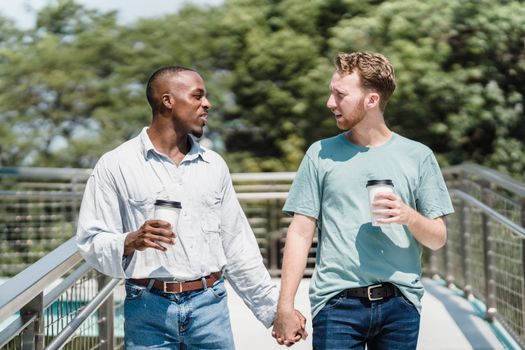 Two men holding hands and enjoying coffee on a sunny day outdoors.