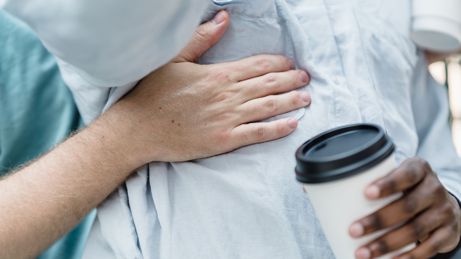 Two adults holding coffee cups and sharing an embrace