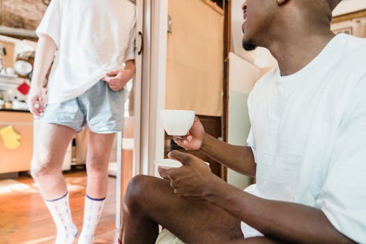 Two men in casual wear enjoying coffee at home, showcasing a relaxed and intimate setting.