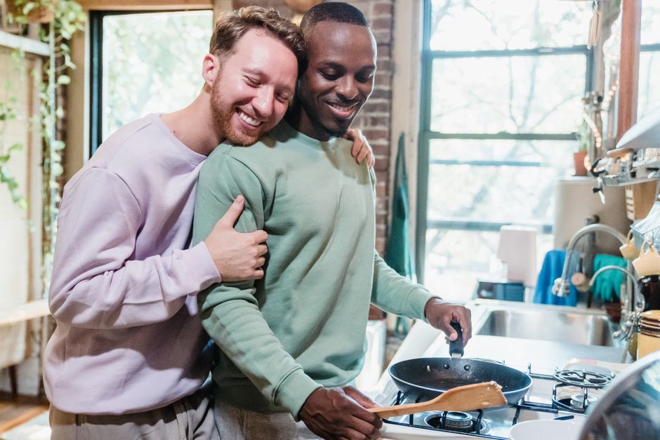 Happy couple cooking in a cozy, sunlit kitchen, sharing a tender moment and laughter.