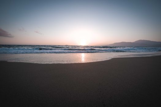 Beautiful sunset over a tranquil beach with gently crashing waves and a sandy shore.