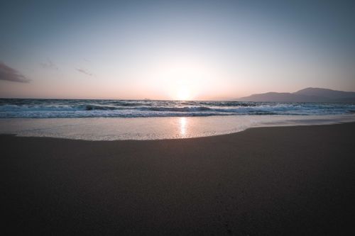 Free Beautiful sunset over a tranquil beach with gently crashing waves and a sandy shore. Stock Photo
