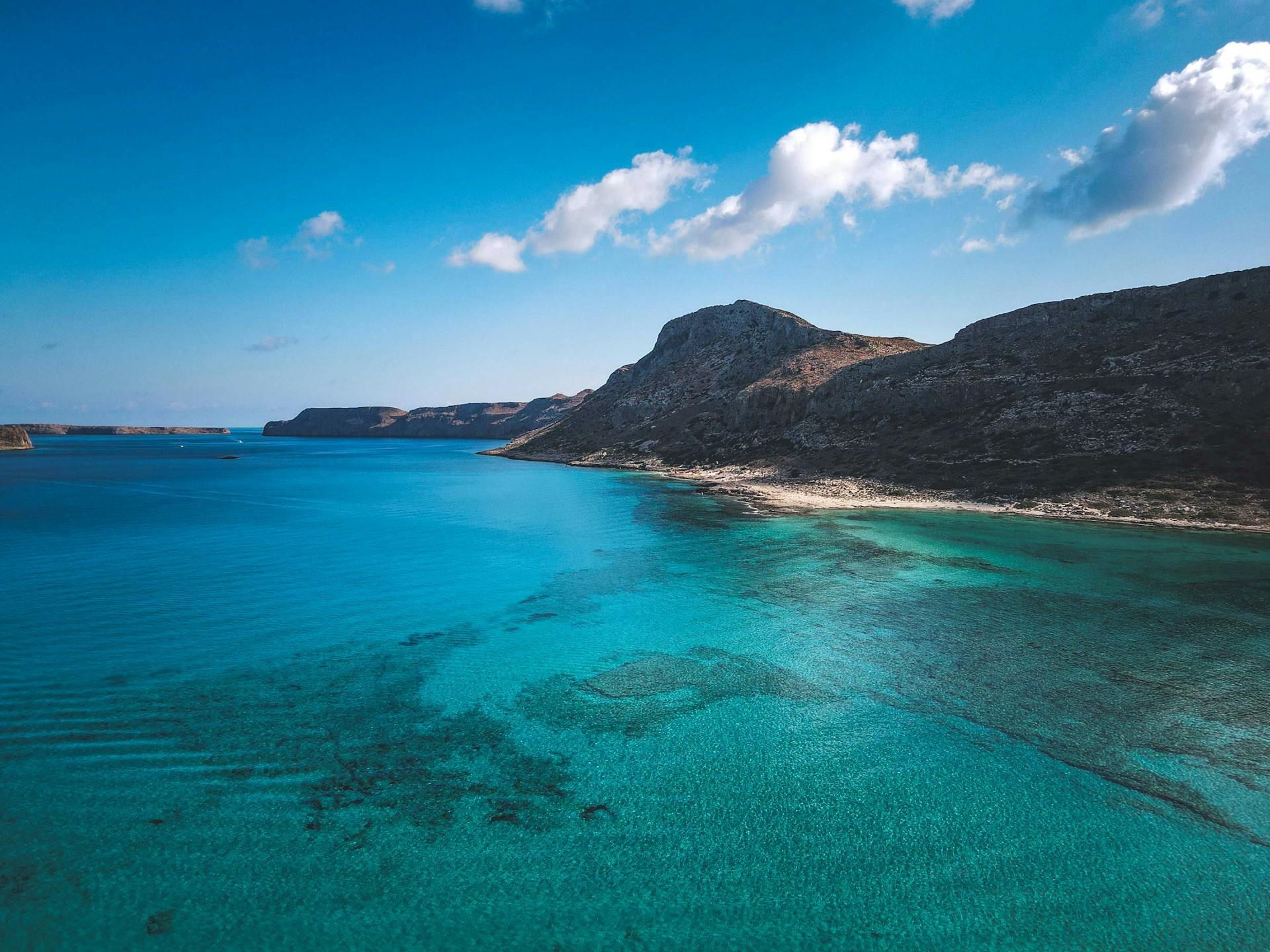 A breathtaking aerial view of a turquoise bay surrounded by rocky cliffs under a clear blue sky.