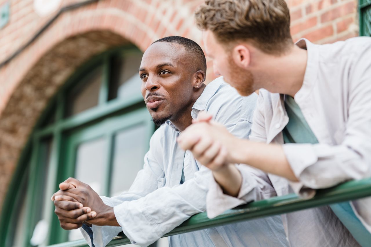two men lean on a railing outdoors engaged in a relaxed conversation