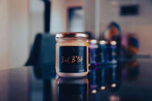 Close-up of a scented candle in a glass jar on a reflective surface. Modern interior setting.