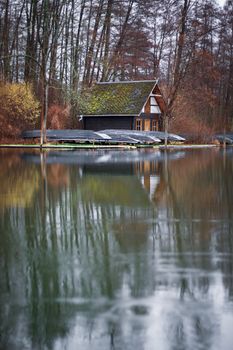 Rustic wooden house with boats reflecting on a tranquil lake in Lübbenau, Germany.