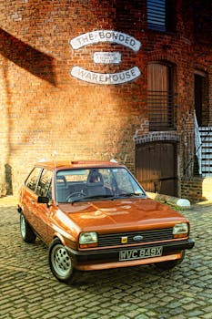 一辆经典的橙色汽车停在一座历史悠久的砖砌仓库前，路面铺着鹅卵石