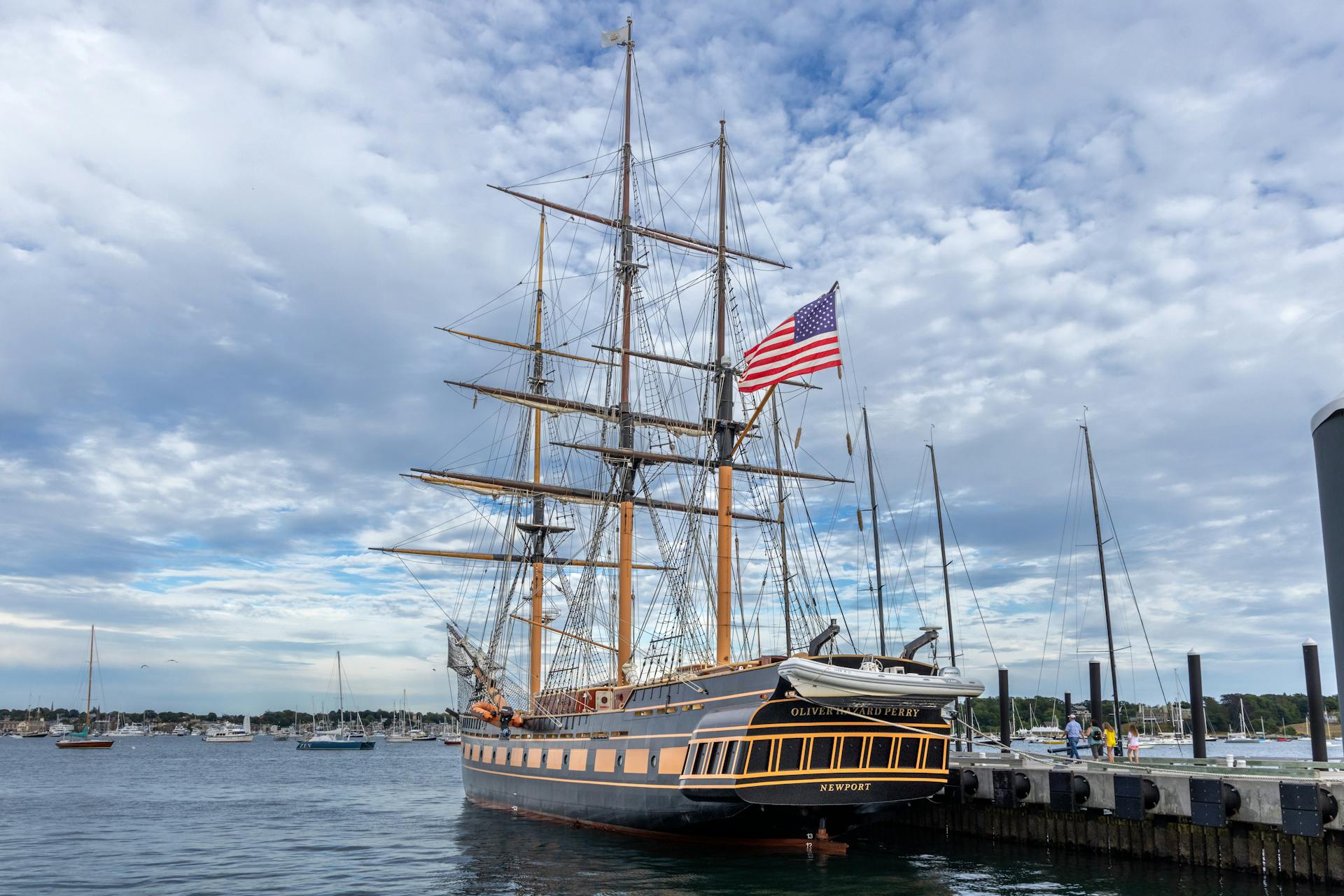 Tall ship with American flag docked at Newport Harbor under a cloudy sky.