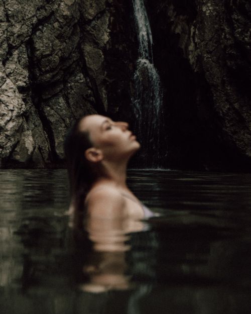 Free Serene scene of a woman relaxing in a secluded waterfall surrounded by rocky cliffs. Stock Photo