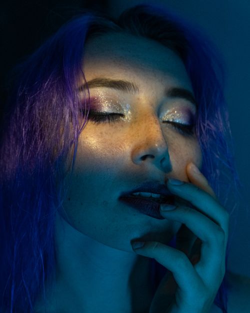 Free A dramatic close-up capturing a woman with purple hair and striking makeup under artistic lighting. Stock Photo