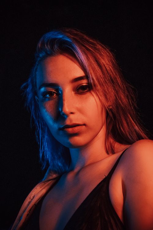 Free Expansive portrait of a woman with dramatic red and blue lighting on a dark background. Stock Photo