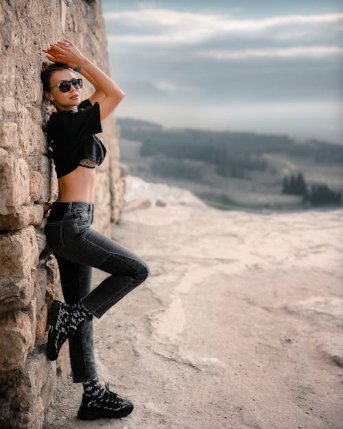 Woman in Black Crop Top and Black Denim Jeans Leaning on Concrete Wall