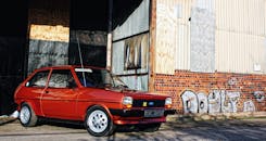 一辆经典的红色掀背车停靠在布满城市涂鸦的墙边，尽显复古风格