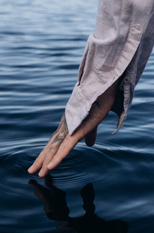 Persons Hand Touching on Body of Water