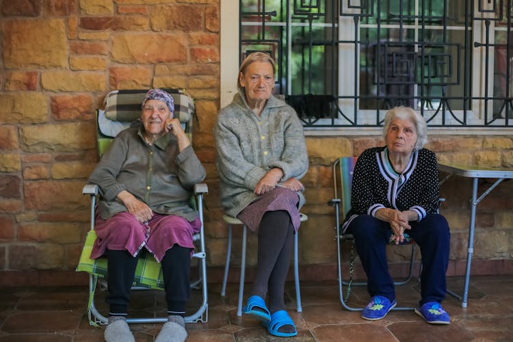 Old Women Sitting In Chairs Near House