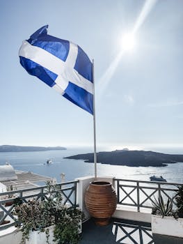 Breathtaking view of the Aegean Sea in Santorini, Greece with a Greek flag waving under the summer sun.