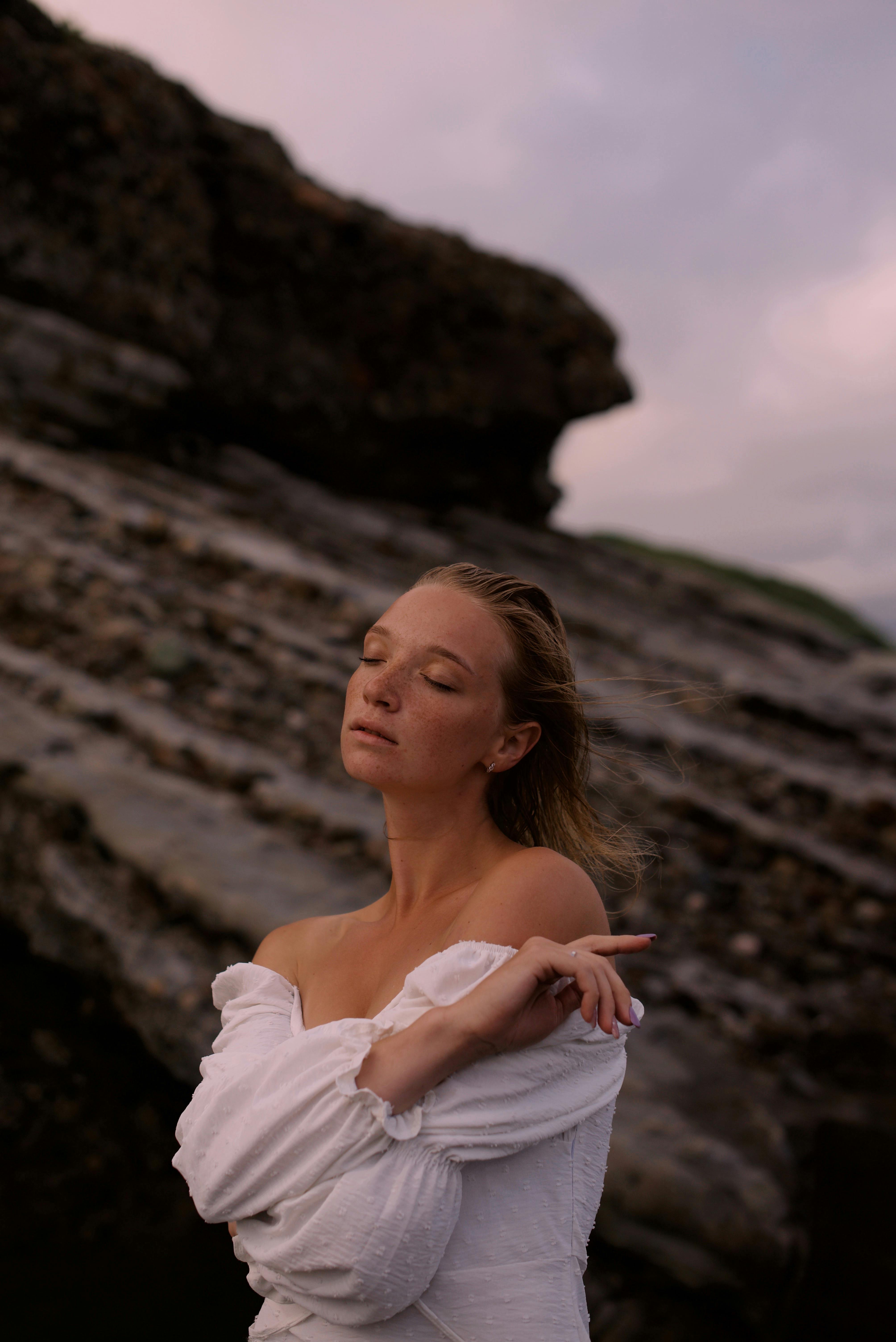 A woman embracing tranquility at a rocky beach during sunset, eyes closed, feeling the freedom.