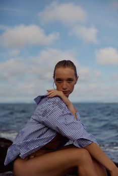 Elegant portrait of a woman sitting by the sea in a striped shirt, exuding natural beauty.