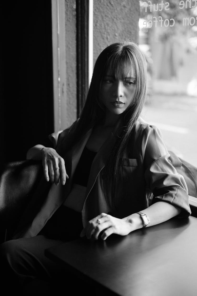 Young Woman Sitting At A Table Next To A Window In A Cafe 