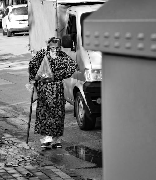 A Grayscale Photo of an Elderly Woman Walking on the Street