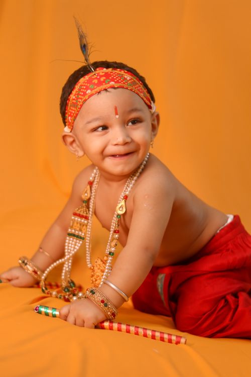 Free Adorable toddler smiling in traditional Indian dress, jewelry, with orange backdrop. Stock Photo