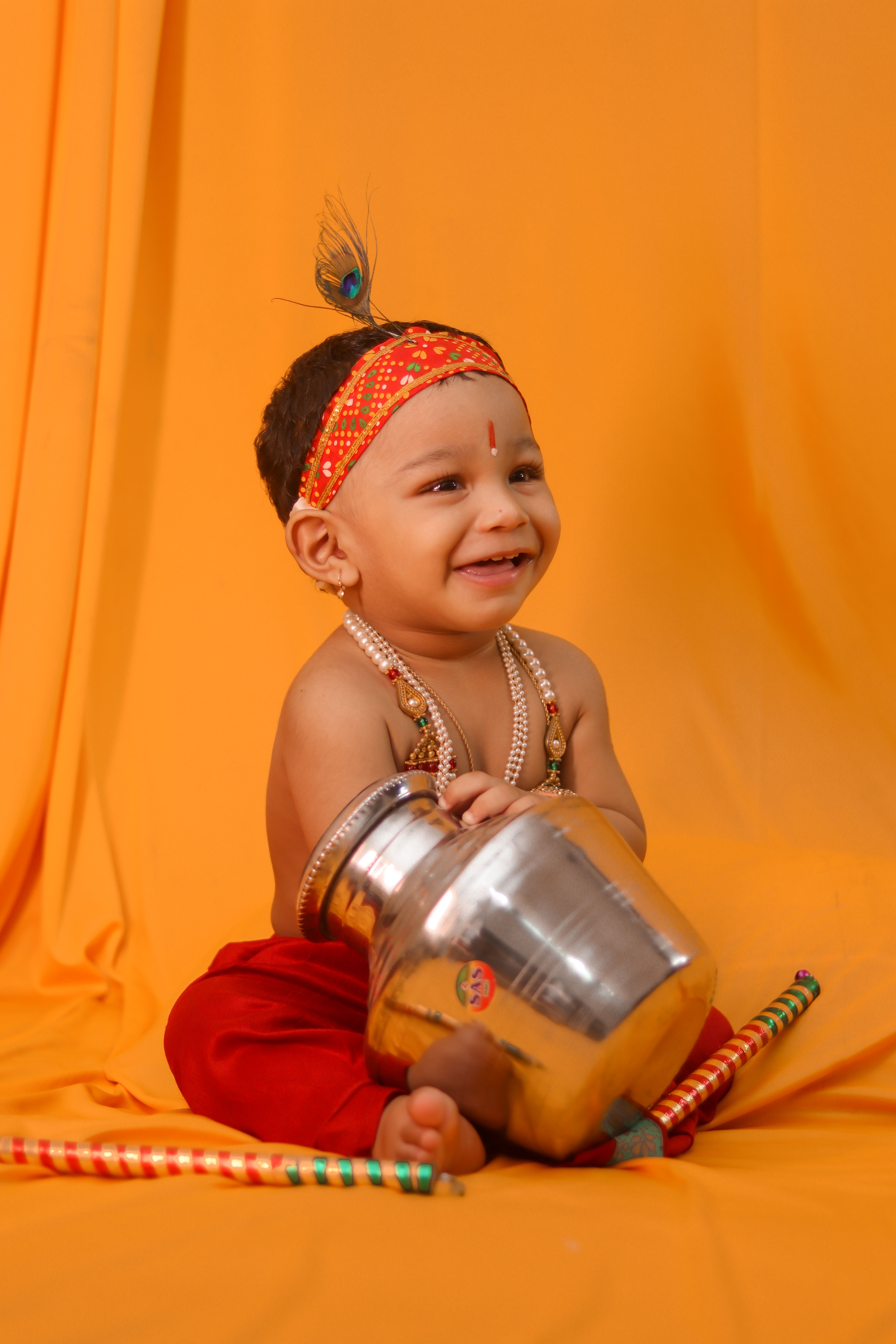 Cute toddler smiling while holding a jar dressed in traditional Indian clothing.