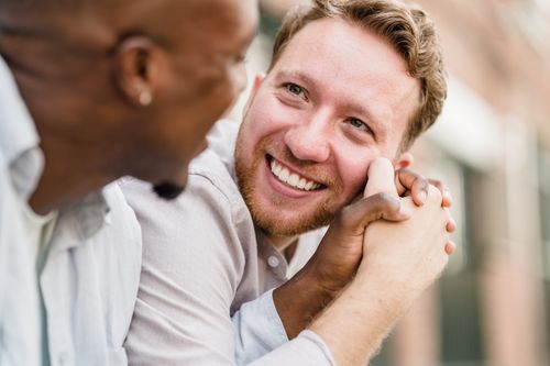 Free Happy couple intimately holding hands and smiling at each other outdoors. Stock Photo
