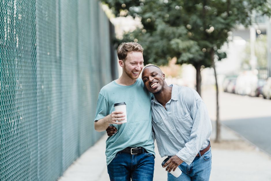 A joyful couple walks arm in arm on a city sidewalk with takeaway coffee cups.