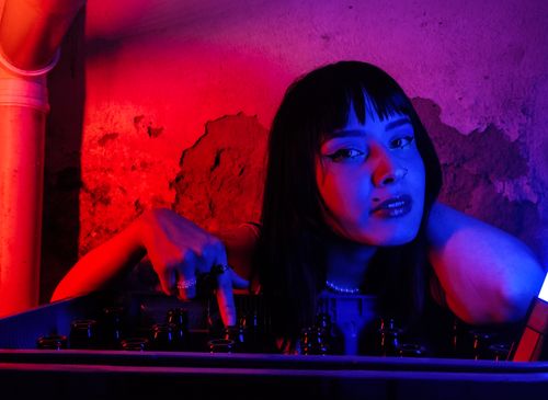 Free A woman in neon-lit room in São Paulo, with red and purple lighting, surrounded by bottles. Stock Photo