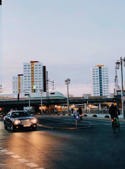An evening urban scene featuring cars, a train, and tall buildings under a twilight sky.