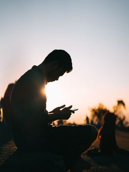 A solitary man in profile silhouetted against a vibrant sunset, focused on his phone.