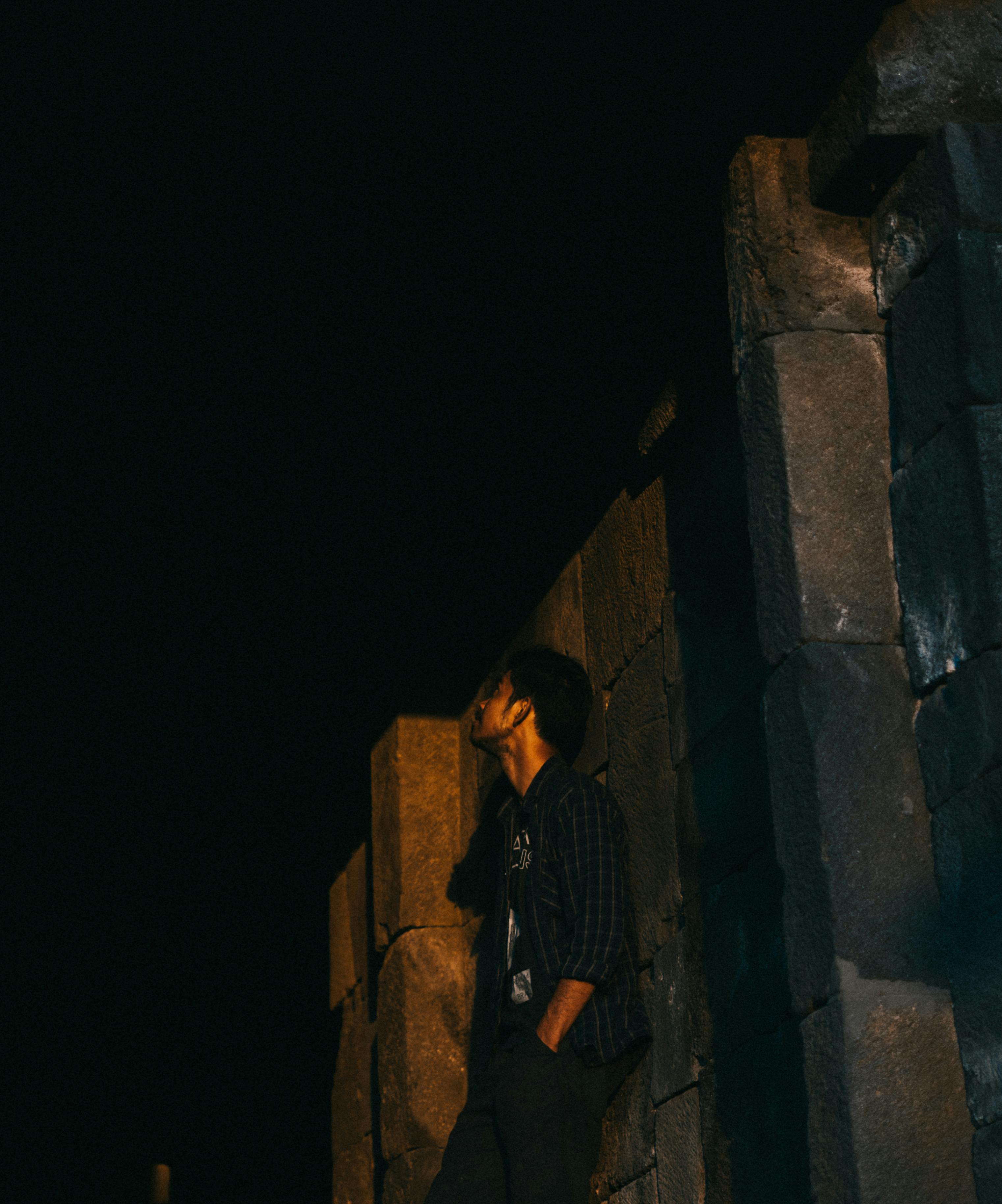 一个男人倚着石墙，仰望夜空沉思