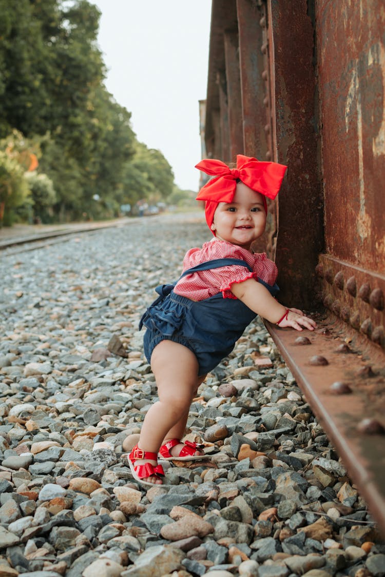 Baby Girl In Blue Denim Romper With Red Ribbon On Head